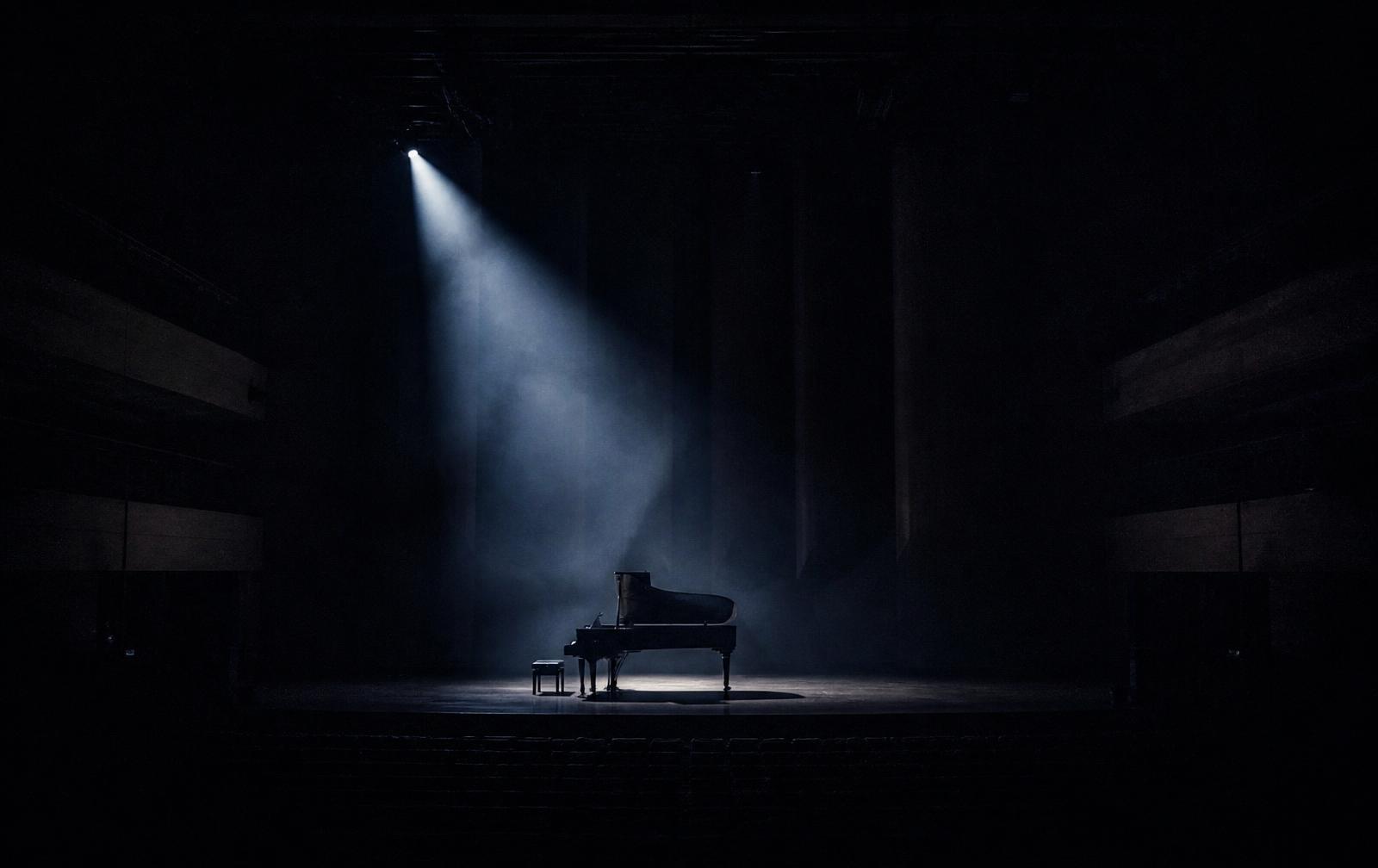 Empty concert hall stage with a single spotlight on a grand piano